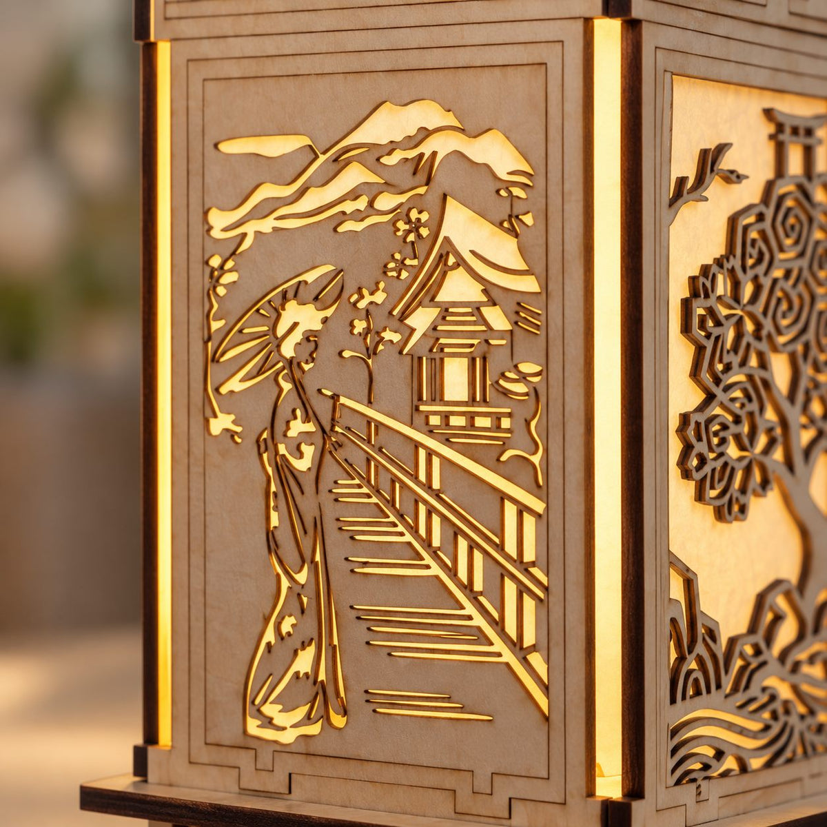 Close-up of the M01 lantern cutout panel showing a parasol figure, bridge, mountain and pavilion with warm light behind the wood