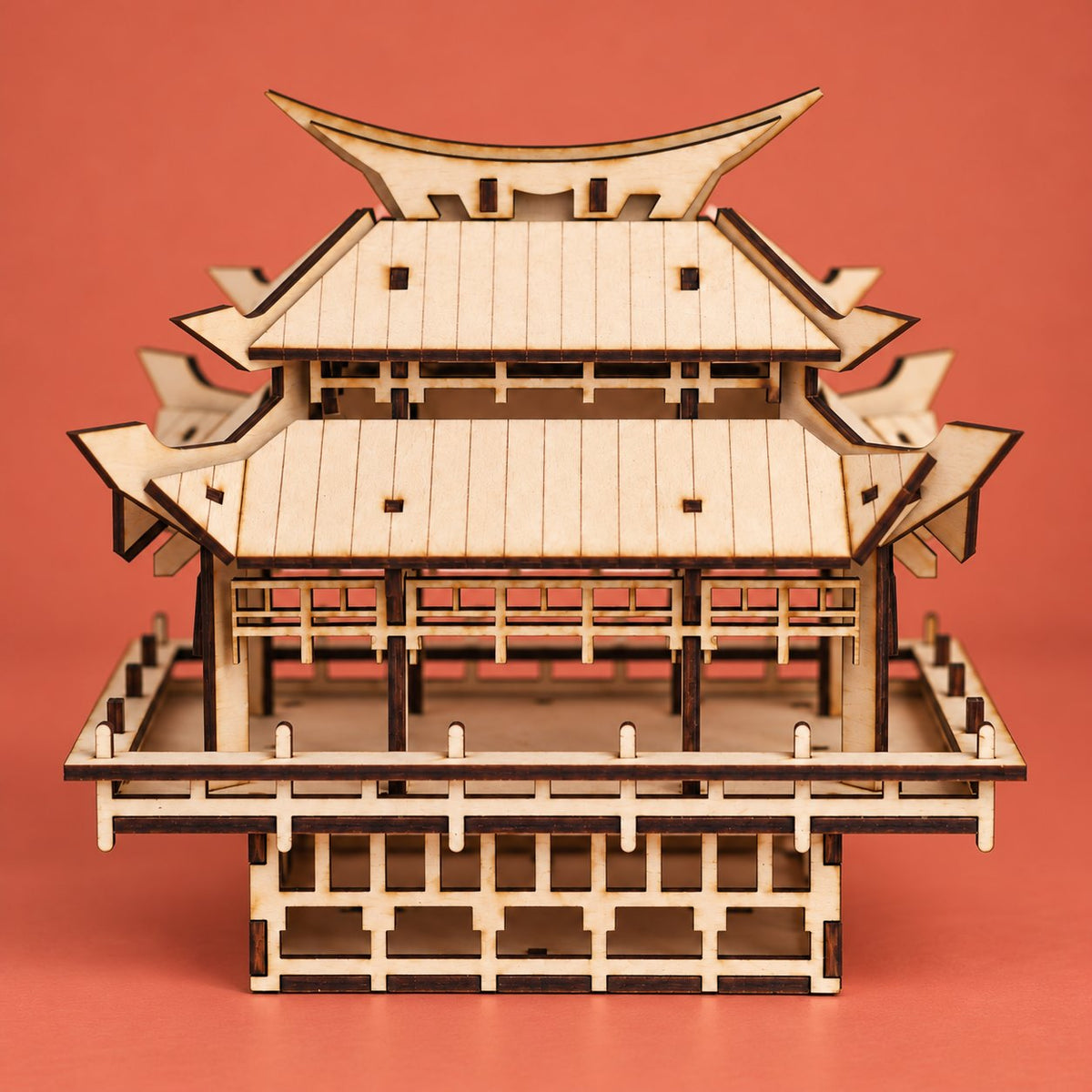 Moonlit wooden pagoda model with layered curved roofs, engraved wood and raised base, full front view on a vibrant warm coral backdrop